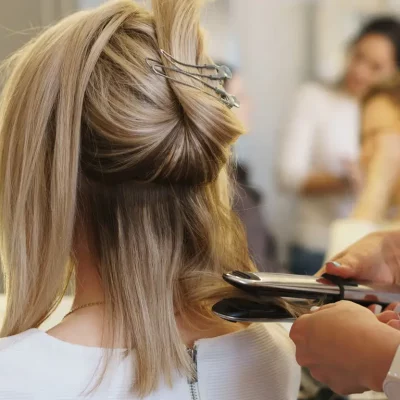 Hairdressing services. Hairtician twirls curls with flat iron hair. Back view. Hairdressing services. Creation of evening hairstyles fashionable stylish women's hairstyles. Hair styling process. Courses in hairdressing. Beauty service concept.